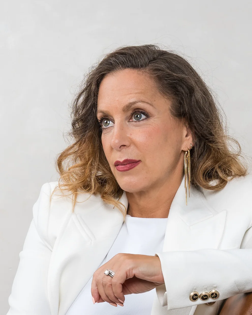 A woman in a white suit, seated, on a pale backdrop