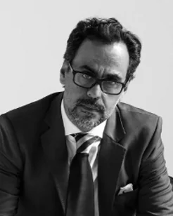 A man in a suit and tie with glasses, seated, black and white