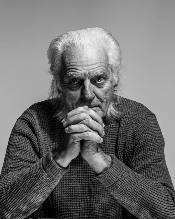 An elderly man, hands clasped, black and white