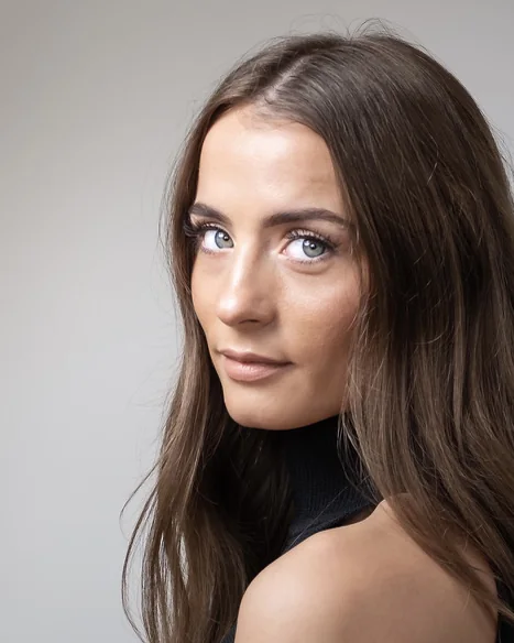 A woman with dark hair looking over her shoulder, grey backdrop