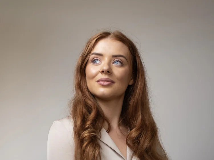 A classic corporate portrait on the grey backdrop: a woman in a cream blouse, soft light, the eyes on the line