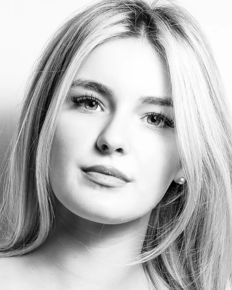 A woman with fair hair in black and white, against a white wall