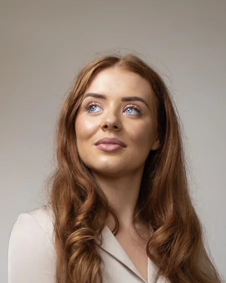 A woman with long red hair on a grey backdrop, looking up