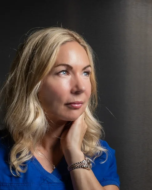 A woman in a blue top, hand at her chin, steel behind